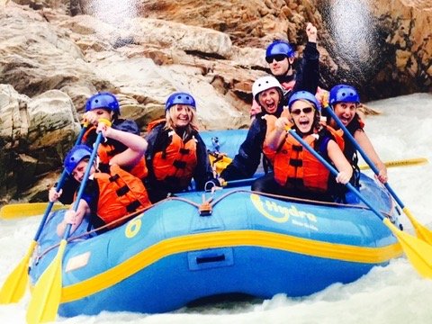 Team white water rafting, paddles raised in celebration